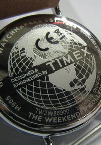 Fond de montre en acier inoxydable argenté présentant un design de globe, le logo "TIMEX" et un texte gravé ; comprend des détails tels que les informations sur le modèle et le marquage CE.
