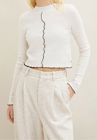 Biały, prążkowany, długi top z krótkim rękawem z falistym czarnym wykończeniem na środku i u dołu, w połączeniu z jasnoszarymi, fakturowanymi spodniami.