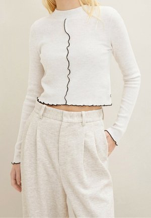 Top corto a maniche lunghe bianco a coste con un bordo ondulato nero al centro e all'orlo, abbinato a pantaloni grigi chiari con una texture.