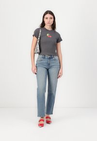 T-shirt cinza com detalhes em relevo apresentando um gráfico de cerejas, emparelhado com jeans reto de perna clara e sapatos de salto alto vermelhos com acabamentos em prata.