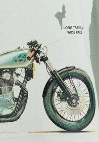 Gráfico de una motocicleta con un tanque plateado, marco negro y radios anchos. El texto indica "Largo recorrido y amplia carrera" cerca del diseño.