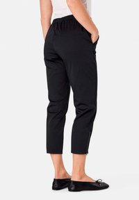 Zwarte enkellange broek met een elastische tailleband, zijzakken en een ritsaccent aan de zoom, gemaakt van soepele, lichte stof.