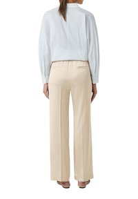 Witte blouse met lange mouwen en een hoge hals, gecombineerd met beige wijde broek. De broek heeft achterzakken en een gladde textuur.