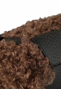 Bolso de cuero negro con una superficie texturizada y acentos de pelo rizado marrón. El diseño combina materiales suaves y peludos.