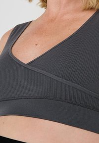 Soutien-gorge de sport gris à côtes avec un design en V, présentant une large bande inférieure et une finition sans couture le long des bords pour un confort accru.