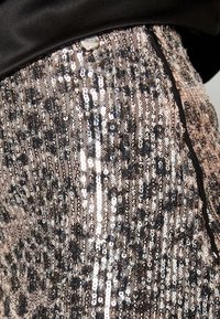 Tessuto decorato con paillettes in tonalità di oro, argento e nero, caratterizzato da una silhouette aderente e una morbida fascia nera nella parte superiore.