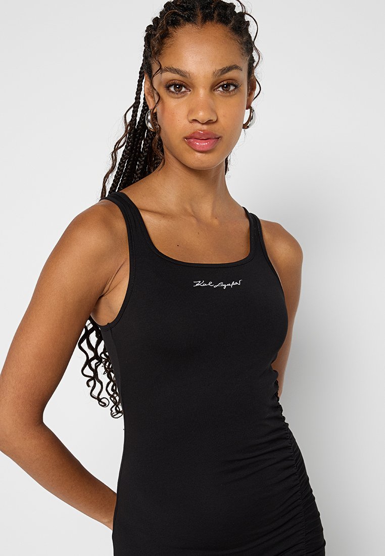 Schwarzes Tanktop mit taillierter Passform, rundem Halsausschnitt und geraffter Seitenstruktur. Mit kleinem weißen Logo auf der Brust.