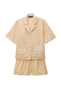 Ensemble de chemise à manches courtes et de shorts de couleur pêche claire, avec des motifs floraux blancs brodés sur les poches avant. Tissu doux, coupe décontractée.