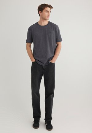 Herren T-Shirt aus dunkelgrauer Baumwolle mit rundem Halsausschnitt und kurzen Ärmeln, kombiniert mit schwarzen Jeans und schwarzen Sneakers. Einfaches Design und lässige Passform.