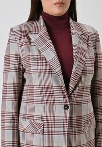 Kariertes Blazer in Beige-, Burgunder- und Blautönen; mit Reverskragen, einem Knopf und zwei Vorderpäcken. Strukturiertem Stoff.