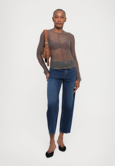 Transparante bruine blouse met lange mouwen, aangesloten en met knopen, gecombineerd met donkerblauwe rechte jeans. Zwarte puntige ballerina's en een bruine tas maken de look compleet.