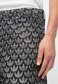 Melnas un pelēkas džinsa bikses ar atkārtotu lapu rakstu. Tās ir aprīkotas ar priekšējo kabatu, metāla pogu un fakturētu audumu.