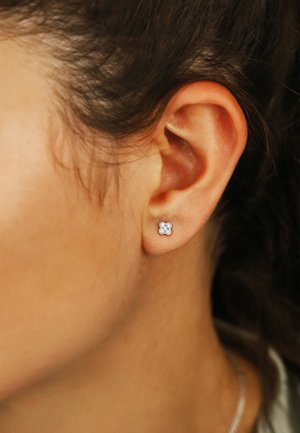 Silberne Ohrstecker in floraler Form mit kleinen klaren Edelsteinen. Nahaufnahme eines Ohrs, die Details und den Glanz des Ohrrings zeigend.