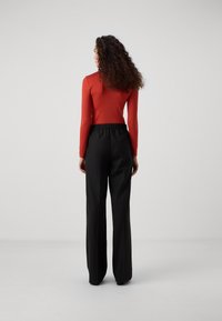 Czerwona, dopasowana bluzka z długim rękawem, zestawiona z czarnymi, wysokim stanem, szerokimi spodniami. Gładka tkanina i elastyczny pasek w talii. Minimalistyczny design.