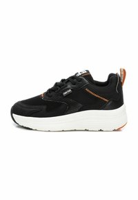 Zapatilla deportiva negra con parte superior de malla y sintético, suela gruesa blanca, costuras de acento naranjas y tab de talón con marca. Paneles texturizados visibles.