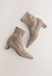 Stivaletti alla caviglia in camoscio beige con punta appuntita, tacco basso a blocco e texture liscia. Dettagli cuciti lungo i lati.