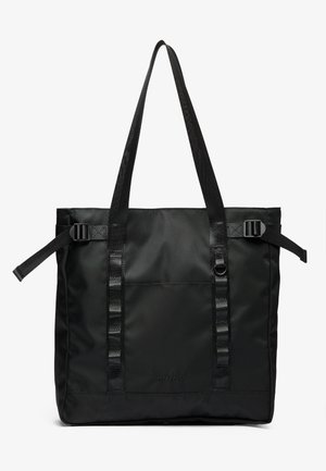 Black tote bag made from durable fabric, featuring two long handles, adjustable straps, and a front pocket. Textured surface with minimal branding.