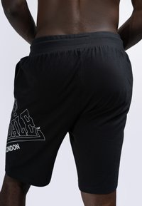 Shorts de sport noirs avec une texture douce, une taille élastique et un logo blanc imprimé sur le côté gauche.