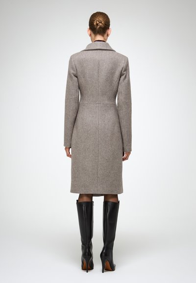 Cappotto in misto lana grigio chiaro, vestibilità su misura con colletto a rever e maniche lunghe, abbinato a stivali a spillo neri in pelle alti.