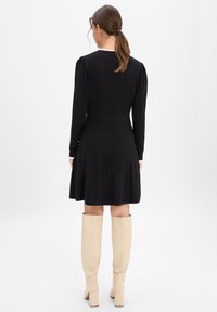 Czarna dzianinowa sukienka z bufkami, prążkowaną fakturą, plisowanym dołem i białym kołnierzem o falistym kształcie. Do tego beżowe kozaki za kolano.