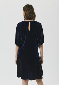 Rochie din catifea bleumarin, cu mâneci scurte tip balon, detaliu cu deschidere pe spate și formă A-line fluidă. Textură moale cu un finisaj neted.
