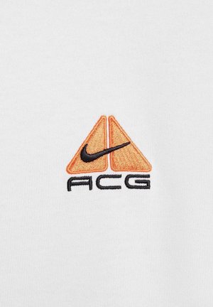 Nike ACG-Logo mit orangefarbenen dreieckigen Formen und schwarzem Text, gestickt auf einem weißen Stoffhintergrund.