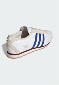 White leather sneaker with blue stripes, beige accents, and a maroon outsole. Features a small brand logo on the heel and textured sole.