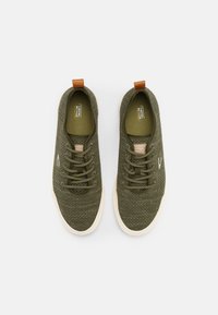 Olivgrüne Canvas-Sneaker mit strukturierter Oberfläche, hellem Gummisohle, runder Zehenpartie und braunem Akzent an der Ferse für einfaches Anziehen.