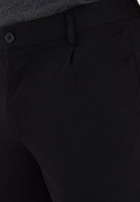 Schwarze Hose aus glattem Stoff, mit einem vorderen Knopfverschluss und subtilen Falten in der Taille für zusätzliche Details.