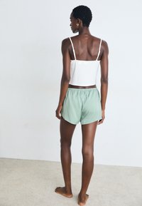Débardeur blanc court avec des bretelles fines, associé à un short à taille élastique vert clair. Tissu lisse avec une coupe décontractée.