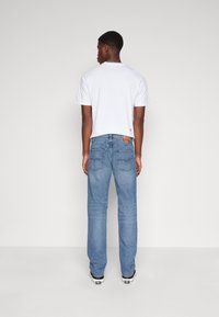 Camiseta blanca de cuello redondo y mangas cortas, combinada con jeans de mezclilla azul claro de corte relajado y bolsillos traseros. Zapatillas negras visibles.