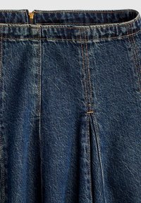 Σκούρα μπλε τζιν φούστα με κεντρική πιέτα και ορατό φερμουάρ στο πάνω πίσω μέρος, διακοσμημένη με πορτοκαλί ραφές.