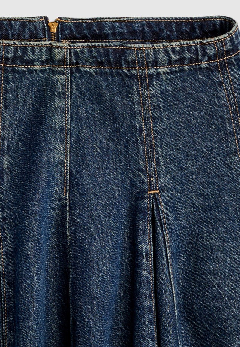 Jupe en jean bleu foncé avec un pli central et une fermeture éclair visible en haut au dos, détaillée avec des coutures orange.