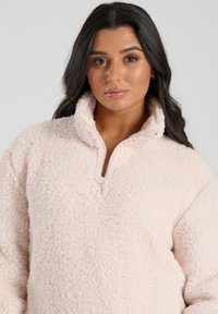 Lyserød fleece-pullover med halv-zipper krave, blød tekstur og en afslappet pasform, der har fluffy, struktureret stof overalt.