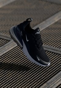 Fekete sportcipő textúrált hálós felsőrésszel, fehér Nike logóval és látható légkamrával. Lekerekített talp kontrasztos szürke részletekkel.