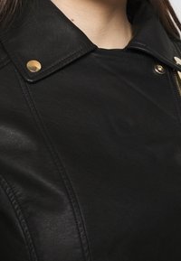 Giacca in pelle nera con colletto a punta, bottoni a scatto dorati e dettagli di cucitura visibili. Texture liscia con un design contemporaneo.
