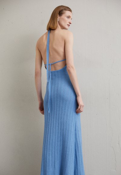 Robe tricotée bleu, côtelée, avec un design de cou halter et un dos ouvert, featuring des bretelles fines et une fente latérale pour faciliter le mouvement.