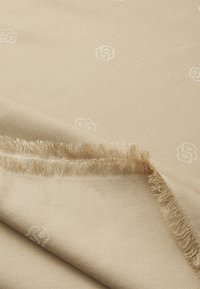 Beige vævet tørklæde med blød tekstur, der har et subtilt logo mønster og frynser i kanterne for ekstra detaljer.
