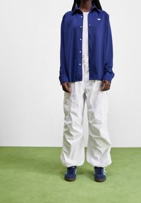 Navy button-up shirt, white t-shirt, white cargo pants, and blue sneakers. Features include a smooth texture and side pockets on pants.