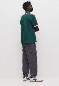 Mørkegrøn t-shirt med hvid krave, kombineret med løse grå cargo-bukser med sidelommer, og hvide sneakers med sorte detaljer.