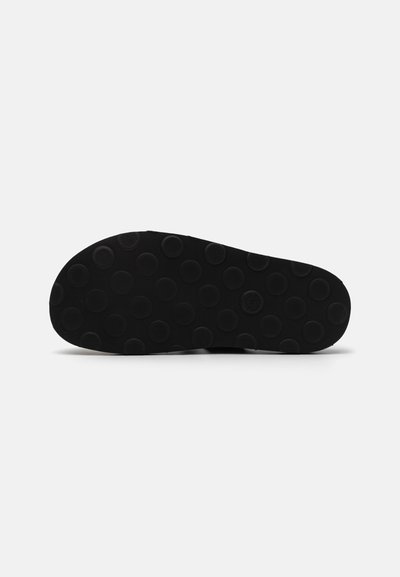Black rubber shoe sole with a flat design and circular tread pattern, featuring raised circular dots for grip and traction.