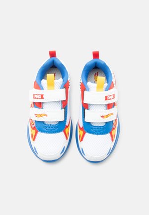 Scarpe da ginnastica bianche da bambino con dettagli blu e rossi, linguette gialle, grafiche a fiamma e due chiusure in Velcro bianche con loghi.