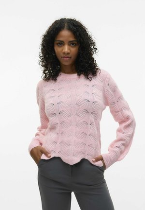Roze gebreide trui met een golfpatroon, geribbelde manchetten en een gegolfde zoom. Gecombineerd met grijze slim-fit broek. Zachte textuur.