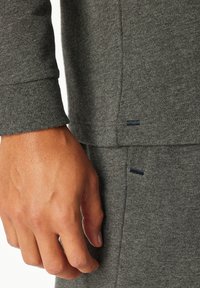 Male hand resting beside gray knit long-sleeve top and matching pants, showing close-up of fabric texture and garment stitching details.