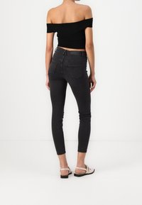 Top negro sin mangas combinado con jeans ajustados gris oscuro. Los jeans tienen una cintura alta, dos bolsillos traseros y una textura suave.