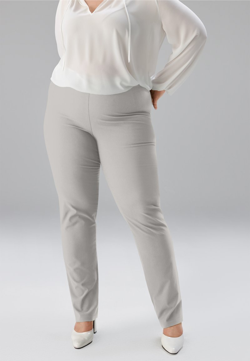Hellgraue, dehnbare Hosen mit schmaler Passform, kombiniert mit einer weißen, locker sitzenden Bluse mit V-Ausschnitt und langen Ärmeln. Glatte Textur.