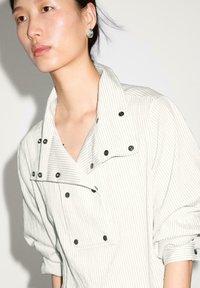 Lys grå stripet skjorte med stor krave, trykknapper og oprullede ærmer. Fremstillet af et tekstureret stof med en subtil glans.