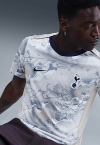 Jersey de Nike de manga corta en gris claro con intrincados patrones de león y pájaro, logo negro y cuello redondo azul marino.
