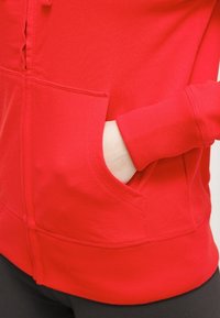 Czerwona bluza z zamkiem błyskawicznym, wykonana z miękkiej tkaniny, z kieszenią kangurzą i ściągaczami na rękawach. Posiada gładką fakturę i dopasowany krój.