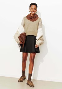 Pull court en laine beige et marron avec manches bouffantes, jupe évasée noire, chaussures à imprimé léopard et sac marron à franges.